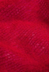 Zbliżenie jasnoczerwonej dzianiny z miękką, puszystą fakturą oraz otwartym, pętelkowym wzorem.