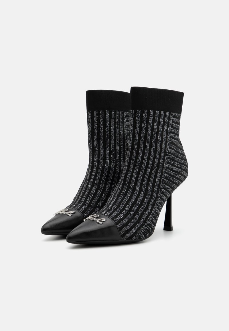 Bottines en tricot avec un motif rayé noir et argent, bout pointu et un capuchon en cuir noir contrastant. Présente des accessoires décoratifs.