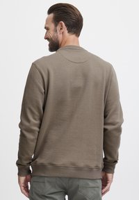 Sudadera de algodón marrón con mangas largas, cuello redondo y puños de canalé. Textura suave con un corte relajado. Costuras visibles y sin logotipos.