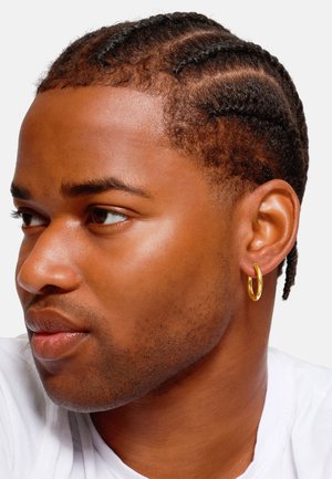 Gold hoop earring on a person with braided hair, light skin, and a neutral t-shirt; focused on the earring's shiny, circular design.