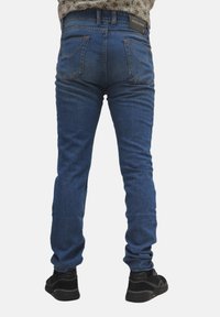 Jeans in denim blu scuro con vestibilità slim, dotati di tasche posteriori e una cintura con marchio. Indossati con scarpe nere, mostrano una silhouette a gamba dritta.