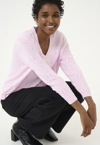 Pull en maille rose pâle avec un col en V et des motifs texturés, associé à un pantalon large noir et des bottines noires à talons carrés.
