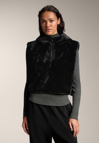 Vest din blana artificiala neagra, cu guler inalt si inchidere cu fermoar, purtat peste un pulover gri cu textura in dungi. Caracteristici notabile includ textura moale si croiala confortabila.