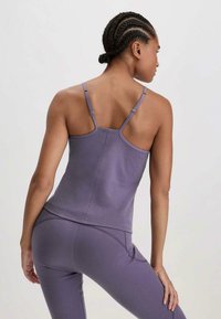 Paars sporttanktop met dunne bandjes, met een aansluitend ontwerp en een zachte textuur, gezien vanaf de achterkant. Bevat subtiele naaddetails.
