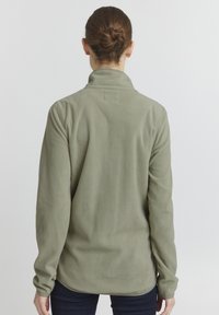 Grønn fleece-pullover med høy krage og lange ermer. Myk tekstur, bakvinkel, har en rett søm og avslappet passform.