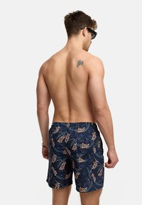 Menns badebukser i marineblått med blomsterdesign i oransje og grønne aksenter. Elastisk midje med snor; lett stoff.