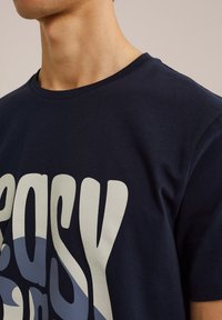 Sötétkék pamut póló nagyméretű, merész "easy" felirattal világoskék és fehér színben. Kerek nyakkal és rövid ujjakkal rendelkezik; puha tapintású.