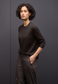 Brązowy sweter z dzianiny o okrągłym dekolcie, w zestawie z luźnymi spodniami w wzór w kratkę, z kieszeniami po bokach.