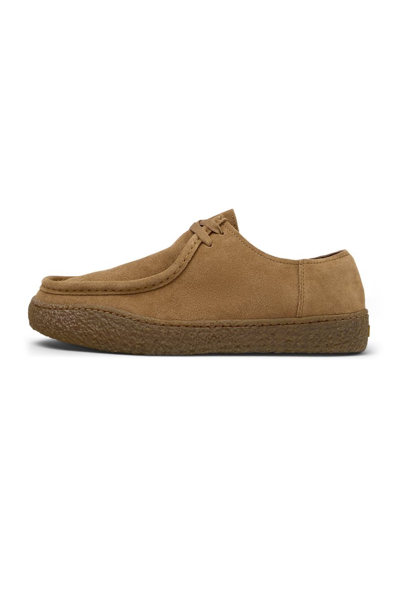 Zapato de ante marrón con puntera redondeada, detalles cosidos y suela de goma marrón texturizada. Presenta un diseño minimalista de cordones en la parte superior.