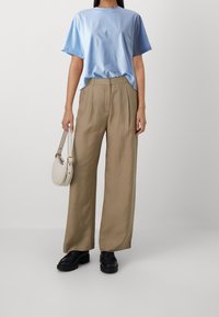 Ljusblå bomulls t-shirt med korta ärmar, kombinerad med beige linnebyxor med vida ben. Handväska i vitt med guldaccenter och svarta skor.