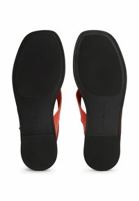 Sandalias de tacón rojo con parte superior lisa, diseño abierto y suelas de goma negra con un patrón texturizado. Logo de la marca grabado en la suela.