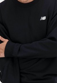 Zwarte sweatshirt gemaakt van een katoenmix, met een geribbelde ronde hals en mouwen. Witte geborduurde logo op de borst, gladde textuur.