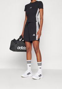 Tenue de sport noire avec des rayures blanches, comprenant un haut ajusté et un short, accompagnée d'un sac de sport Adidas noir et blanc et de chaussettes.