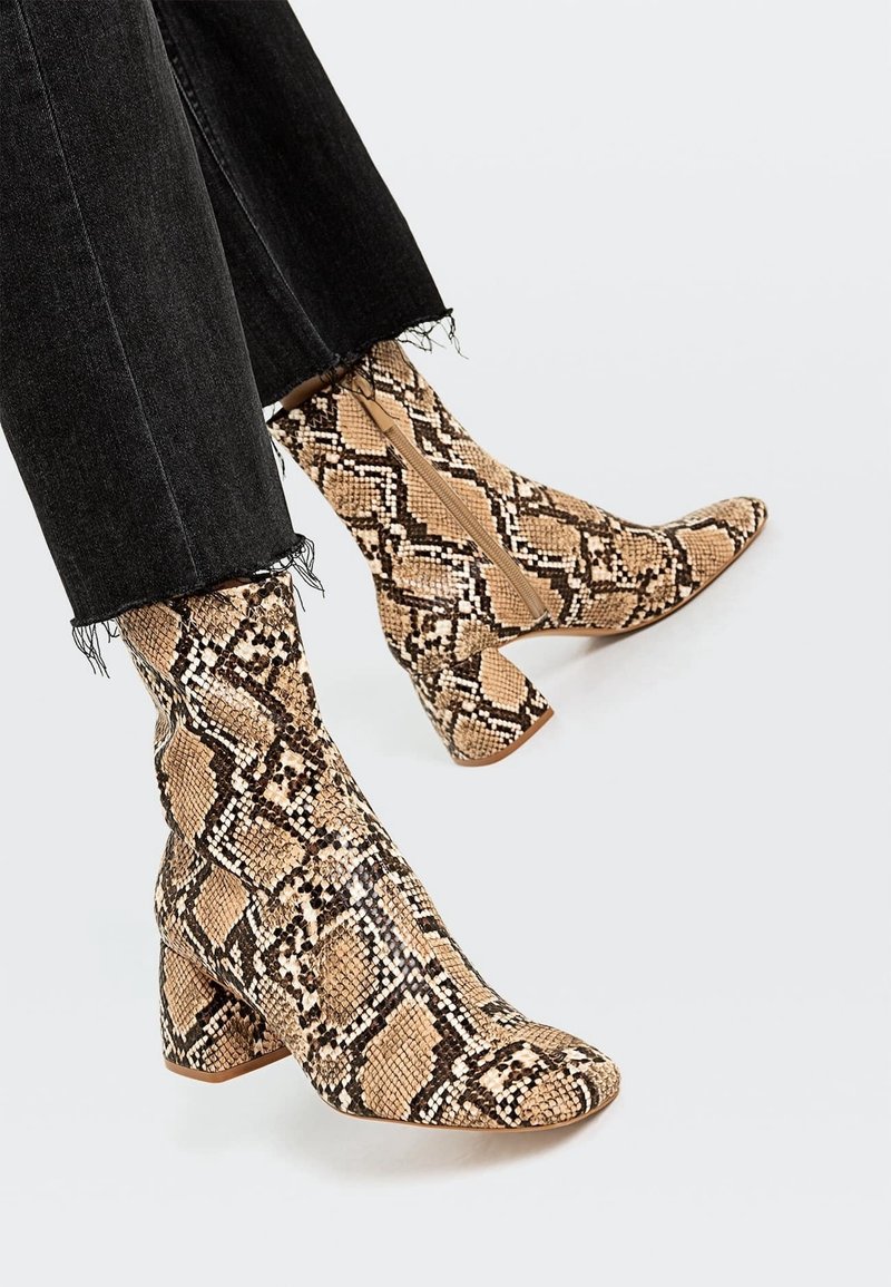 Pieds portant des bottes mi-mollet à bout pointu avec un motif peau de serpent beige et noir et des talons carrés, associées à un jean noir effiloché.