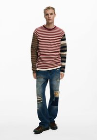 Striped long-sleeve shirt in red and brown tones with varying stripe widths; distressed denim jeans with patchwork detailing and loose fit.
