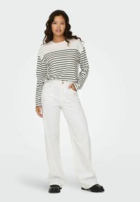 Stribet langærmet top i hvid og sort, parret med højtaljede hvide vide jeans. Outfittet har en afslappet pasform og glat stof.