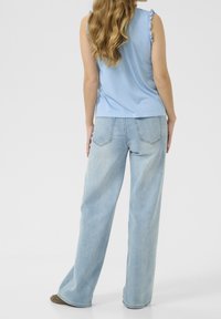 Hellblaues Tanktop mit Rüschenträgern, kombiniert mit hellblauen weiten Jeans. Einfaches Design, weicher Stoff und lässige Passform.