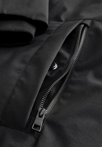 Czarna kurtka wykonana z gładkiego materiału, z widocznym zamkiem błyskawicznym i zapięciem na guziki. Wyróżnia się eleganckim projektem i czystymi liniami.
