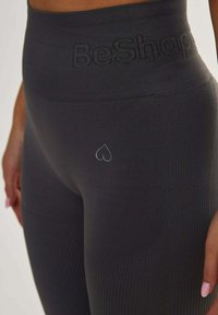 Tightsit, korkealla vyötäröllä, tummanharmaat legginsit, joissa on ribbipinta ja "BeShape"-logo vyötärönauhan kohdalla. Pieni sydänkoriste vyötärön lähellä.