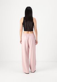 Pantaloni ampi rosa chiaro con vita elastica e una texture morbida, abbinati a un top aderente nero senza maniche.