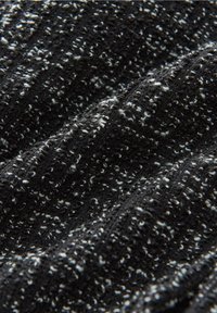 Tissu tricoté en noir et blanc avec une surface texturée, présentant un mélange de motifs mouchetés et de lignes côtelées. Matériau doux et extensible.