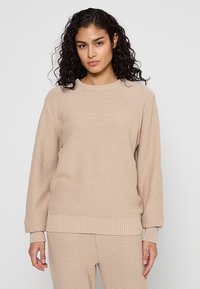Beige gestrickter Pullover mit strukturiertem Muster, Rundhalsausschnitt, langen Ärmeln und geripptem Saum. Lässige Passform, kombiniert mit passenden Hosen.