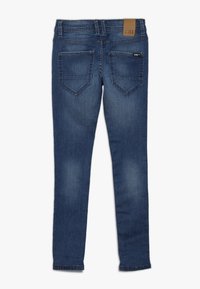 Modré džíny úzkého střihu s hladkou texturou, které mají dvě zadní kapsy a hnědý kožený štítek s logem na pásku.