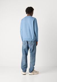 Sudadera azul claro con escote redondo y puños acanalados, combinada con jeans azul claro de corte relajado y zapatillas de color claro.