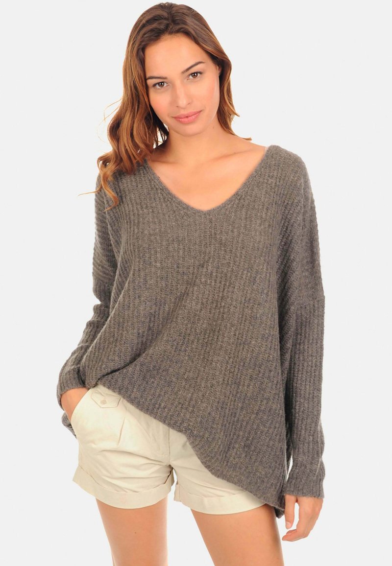 Sweater gris côtelé avec un col en V profond, des manches longues et une coupe décontractée, associé à un short de couleur claire. Matière en tricot texturé.