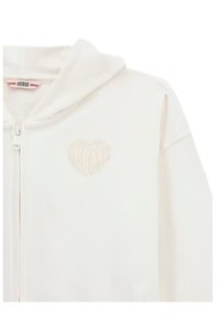 Weißer Reißverschluss-Hoodie mit weichem Material, der ein dezentes Herzdesign auf der Brust und eine Kordelzugkapuze hat.