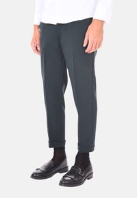 Pantaloni tailored grigio scuro con una texture liscia, dotati di gamba affusolata e risvolti, abbinati a scarpe slip-on in pelle nera.
