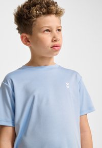 Ljusblå kortärmad t-shirt i slätt tyg med en vit chevron-logotyp på bröstet, rund halsringning och avslappnad passform.
