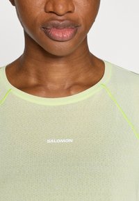 Πράσινο αθλητικό μπλουζάκι κατασκευασμένο από ελαφρύ, υφασμένο ύφασμα. Διαθέτει στρογγυλή λαιμόκοψη, αντίθετη ραφή σε ανοιχτό πρ άσινο χρώμα και λογότυπο "SALOMON" σε λευκό.