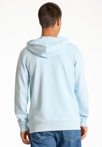 Sudadera azul claro hecha de tejido suave, con un bolsillo tipo canguro, capucha ajustable y mangas largas. Diseño casual con puños acanalados.