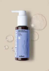 Gel-Serum in einer braunen Glasflasche mit einem weißen Pumpkopf. Auf dem hellblauen Etikett sind Texte und Wellenmuster abgebildet. Klare Gel-Tropfen liegen in der Nähe.