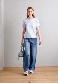 Lyseblå bomull T-skjorte med tekst, sammen med vide, falmede blå jeans. Tilbehør: liten grå håndveske. Fottøy: hvite joggesko.
