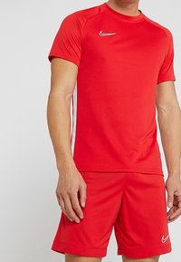 Camiseta deportiva roja de Nike con mangas cortas, cuello redondo y un logo blanco. Combinada con pantalones cortos rojos a juego con acentos laterales.