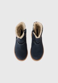 Marineblå ankelstøvler i ruskind med en faux fur-foring, syet detaljer og en brun gummisål. Har en lynlåslukning på siden.