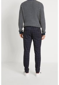 Navy patterned sweater with white motifs, paired with navy checked trousers. Trousers feature a subtle grid design and back pockets. White sneakers.