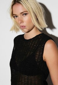 Black sleeveless top featuring a textured knit pattern, with a round neckline and sheer fabric, creating a layered effect.