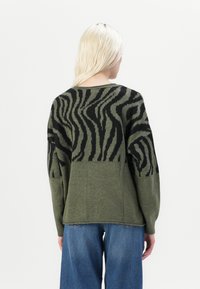 Grüner Pullover mit einem schwarzen Zebra-Streifenmuster, lässiger Schnitt, langen Ärmeln und Rundhalsausschnitt. Glatte Stricktextur.