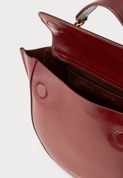 Ανοιχτή σκούρα κόκκινη δερμάτινη τσάντα με μαγνητικό κούμπωμα και στρογγυλεμένες άκρες που δείχνει την εσωτερική τσέπη με την ετικέτα Wandler, φτιαγμένη στην Ιταλία.