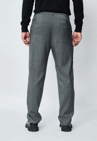 Pantalon gris sur mesure avec un motif à carreaux subtil. Comprend deux poches arrière, coupe slim, et est associé à des chaussures noires.