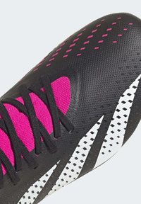 Mustat ja vaaleanpunaiset jalkapallokengät, joissa on teksturoitu pinta, mustat nauhat sekä valkoiset raidat korostuksina ja rei'itykset hengittävyyden parantamiseksi.