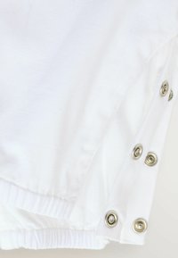 Tissu blanc avec un motif texturé subtil, accompagné de boutons-pression en métal argenté le long du bord et d'un ourlet élastiqué.