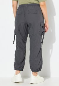 Cargo-broek in donkergrijs nylon met elastische boorden, voorzien van dubbele achterzakken en zijcargozakken, gecombineerd met witte platform sneakers.