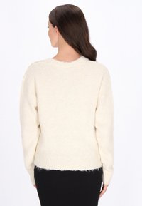 Krém színű pulóver, amely kényelmes kötött textúrával rendelkezik, hosszú ujjak, kerek nyakú és bordázott alsó résszel. Puha és laza fazon.