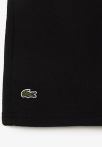 Musta puuvillapaita, jossa on pieni vihreä krokotiililogo kirjottuna alakulmaan. Paidassa on sileä pinta ja tavallinen leikkaus.