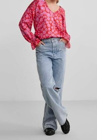 Blusa rosa brillante con maniche a palloncino e motivi a forma di cuore, abbinata a jeans larghi strappati blu chiaro e scarpe nere.