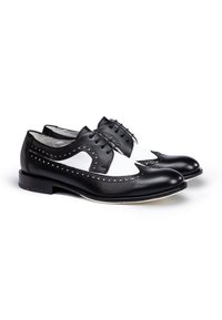 Des oxfords en cuir noir et blanc avec un bout pointu, des détails perforés, des panneaux contrastants, et un petit talon pour un style formel.